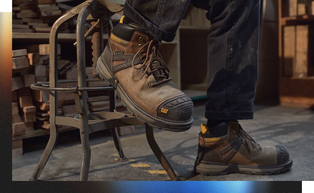 A person's feet in a chair wearing CAT Work Boots.