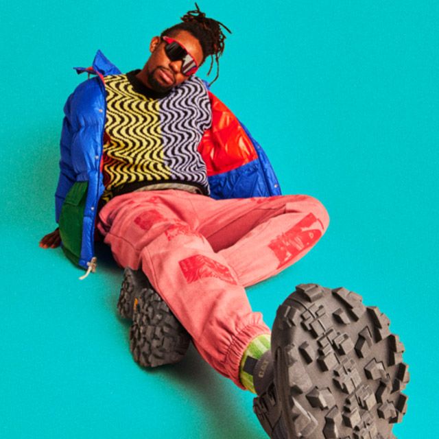 A person sitting on a blue background wearing CAT Intruder shoes.