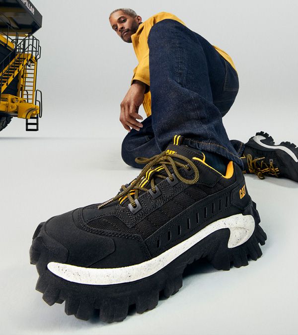 A person sitting on the ground wearing CAT footwear Intruder Shoe black and white.