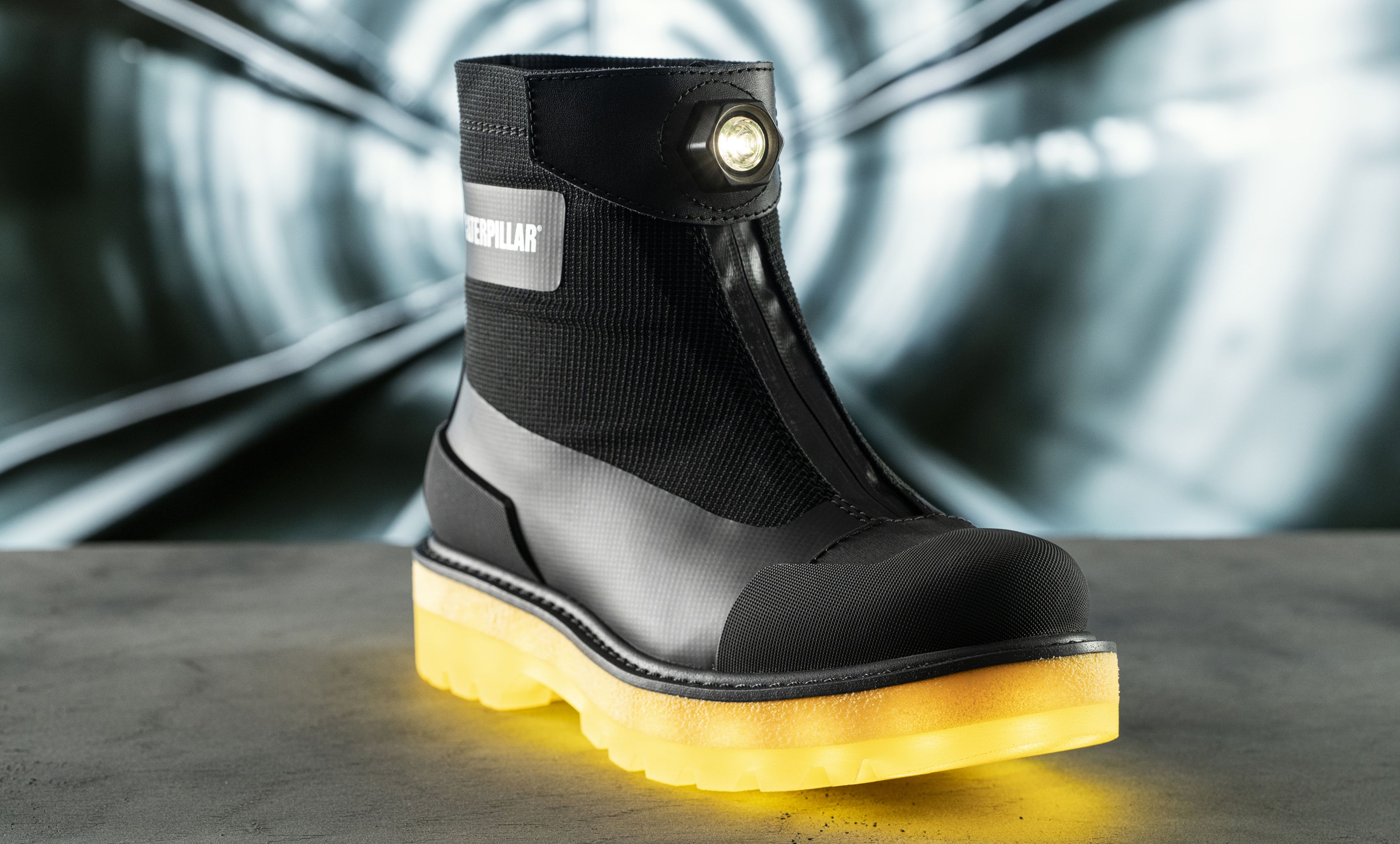A self-illuminated black boot with a yellow sole in front of a tunnel entrance.