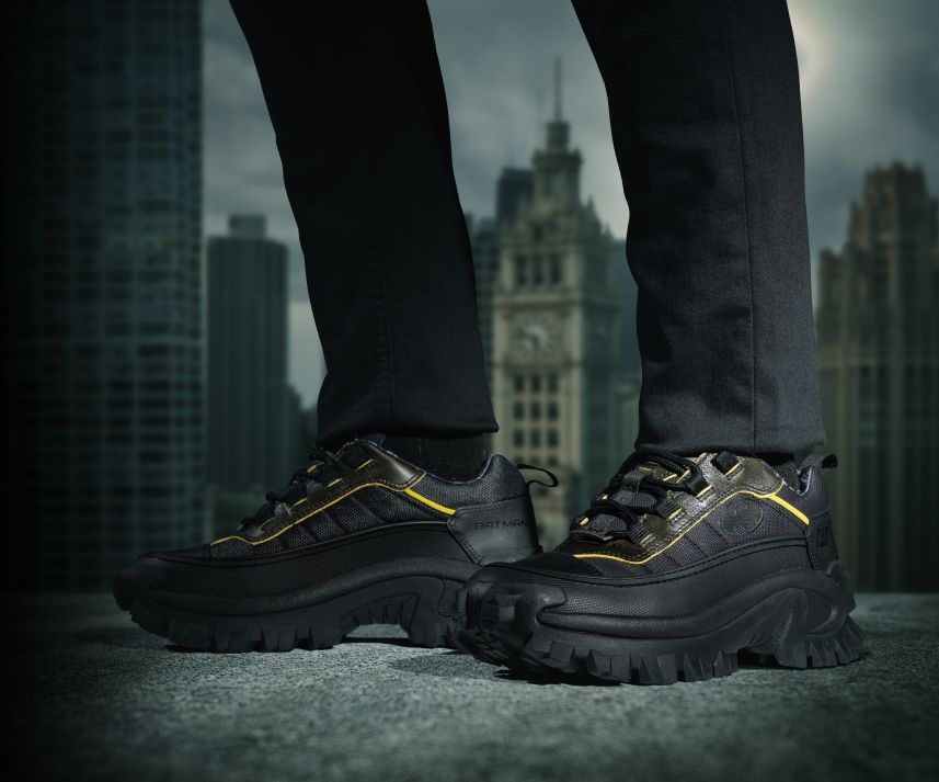 Black & yellow shoes with Batman logo walking on a precarious city ledge.