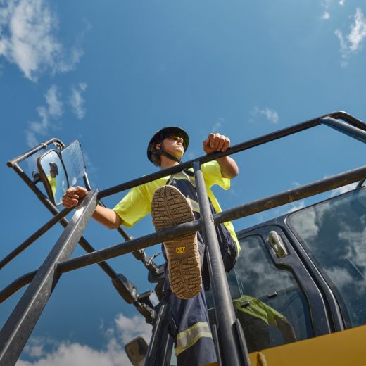 Looking up at a worker against the sky standing on the tracks of heavy machinery.
