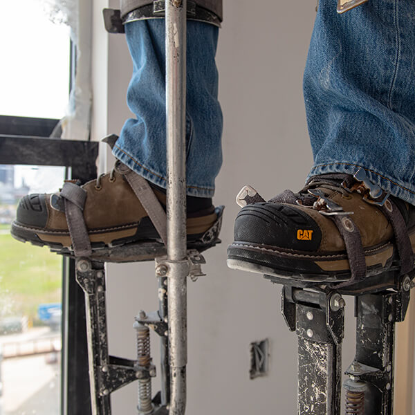 Boots standing on a pair of drywall stilts.