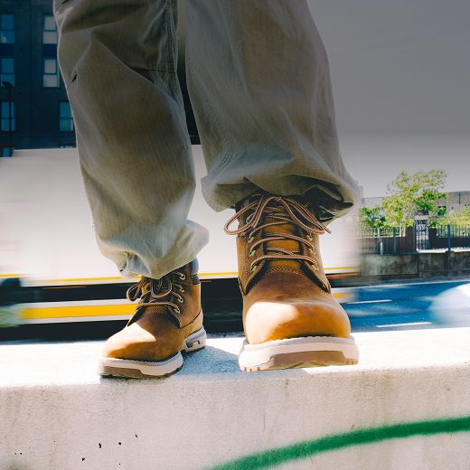 Brown boots standing on a concrete wall beside an urban road.