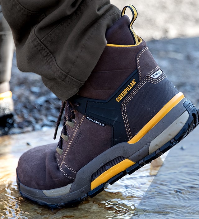 A person walking at a work site, wearing CAT Edge boots.