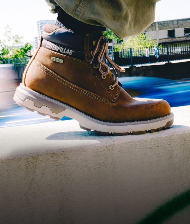 Brown boots walking along a concrete wall.