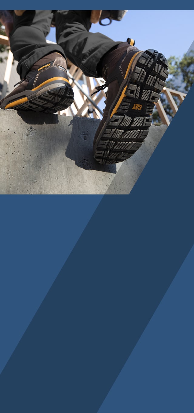 A person walking up concrete steps at a work site, wearing CAT Edge boots.