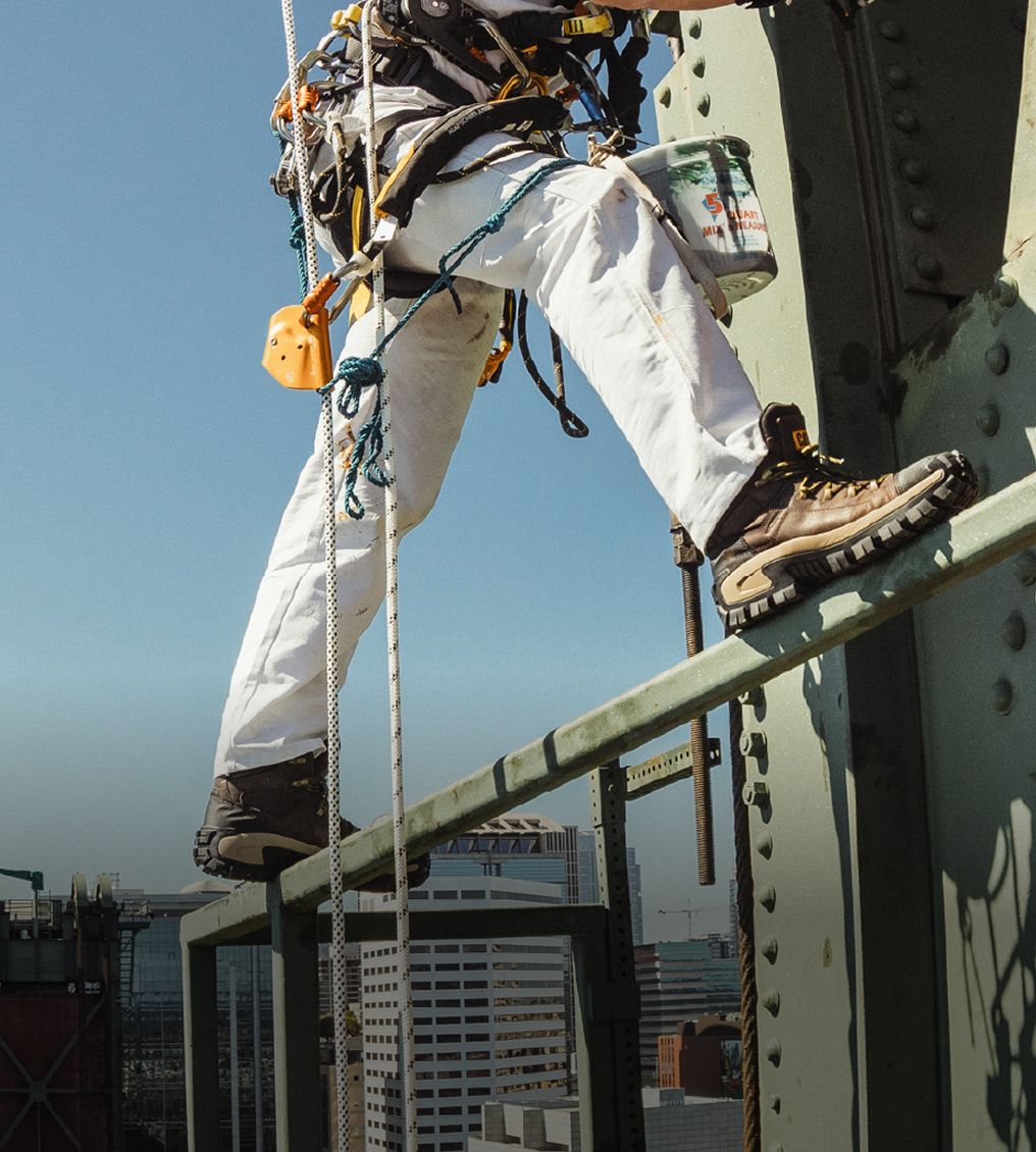 Boots standing on narrow steel framing above a city skyline.