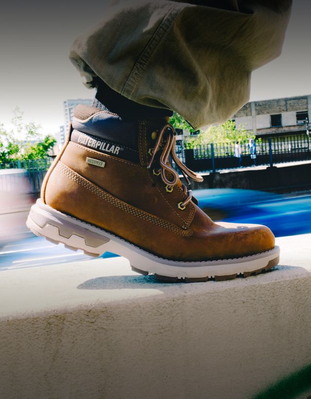 Brown boots walking along a concrete wall.