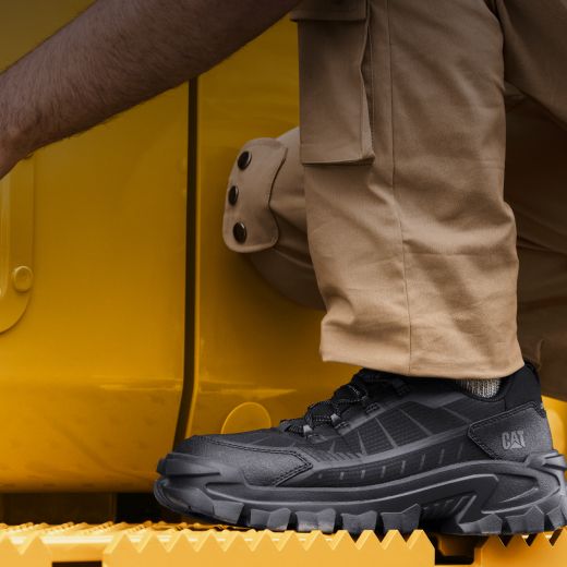 Black boots standing on the footplate of heavy Caterpillar machinery.
