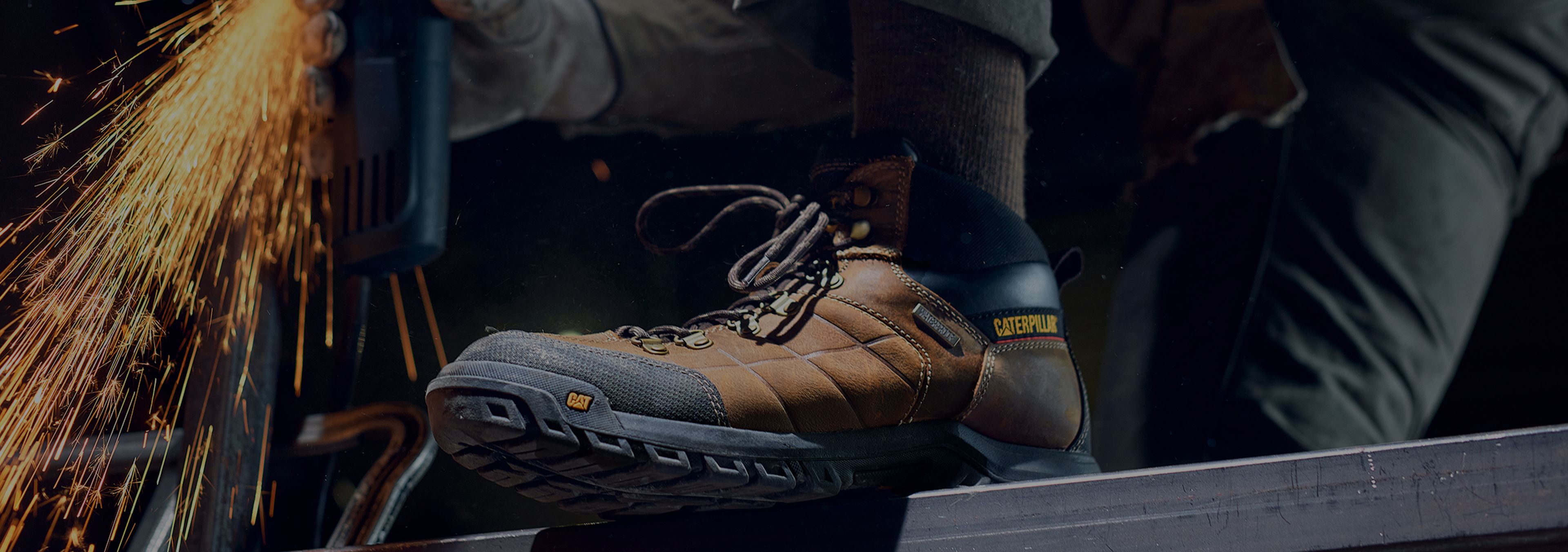 Sparks from an angle grinder behind boots standing on a steel beam.